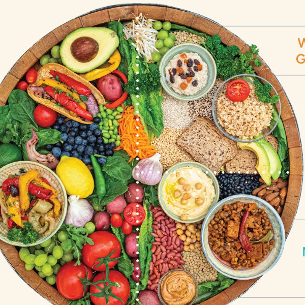 A round harvest board of whole plant foods — legumes, whole grains, vegetables, fruit, and nuts